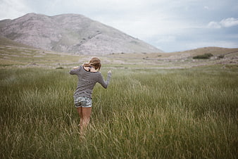 Woman Walking Through Tall Grass in Mountain Landscape