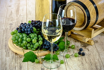 Red and white wine glasses with fresh grapes on wooden table