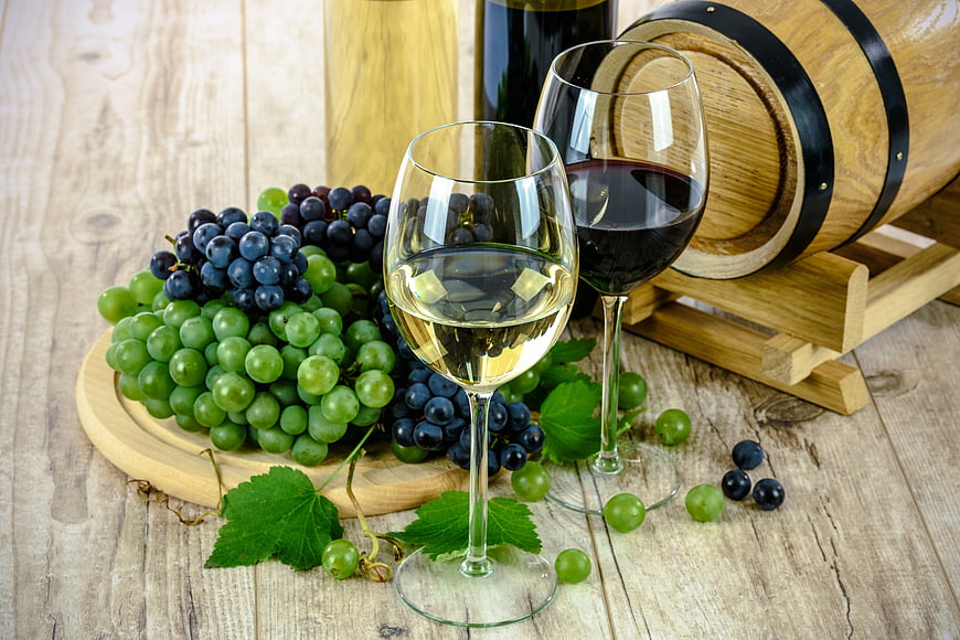 Red and white wine glasses with fresh grapes on wooden table
