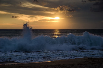 Dramatic ocean waves crashing on beach at golden sunset