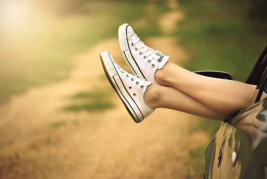 Relaxed legs in white sneakers hanging from car window