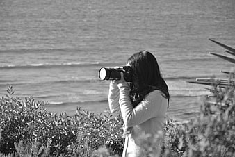 Woman photographer taking photo by the ocean in black and white
