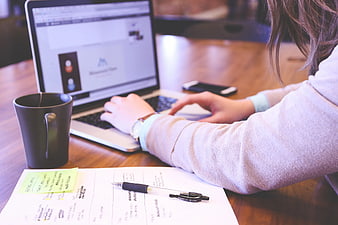 Woman Typing on Laptop at Wooden Desk with Coffee