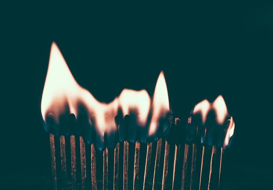 Row of lit matches burning against dark teal background