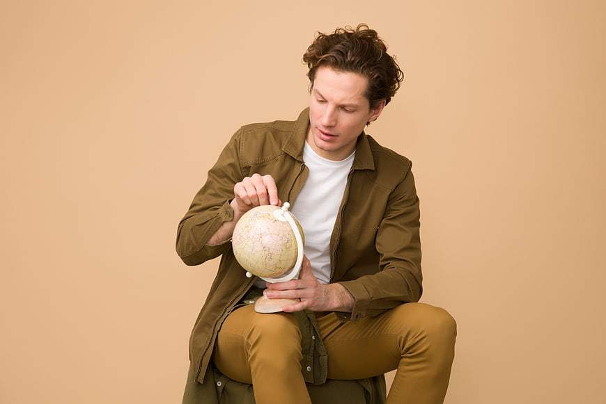Young man sitting and holding a globe against beige background