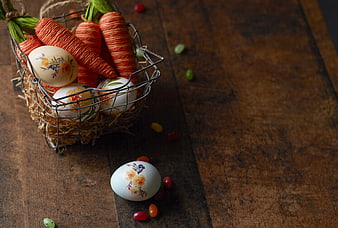 Easter eggs and yarn carrots in wire basket on wood