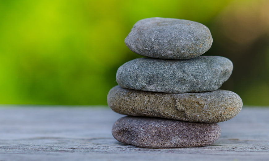 Stacked smooth stones on wooden surface with green background