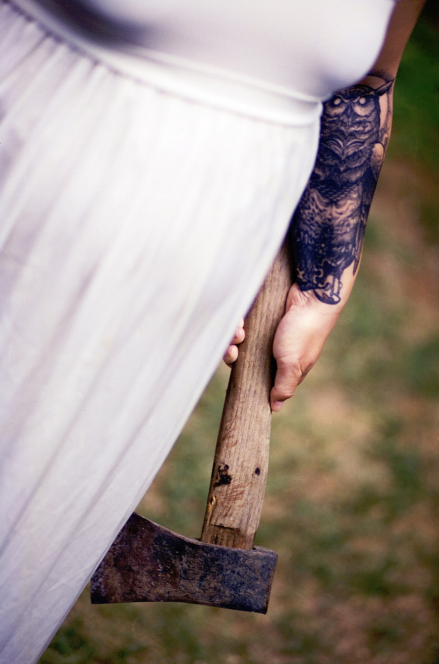 Woman with owl tattoo holding rusty axe outdoors