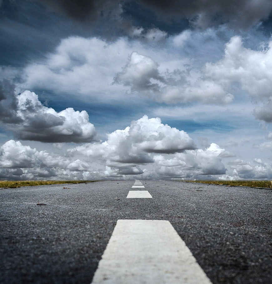 Low angle view of empty asphalt road under dramatic cloudy sky