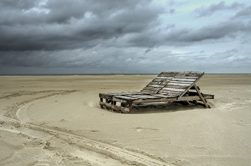 Weathered Wooden Beach Chair on Sandy Shore Under Stormy Sky