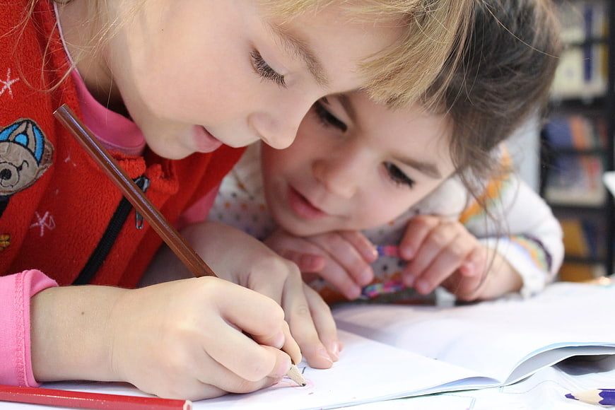 Two young girls drawing together in a notebook