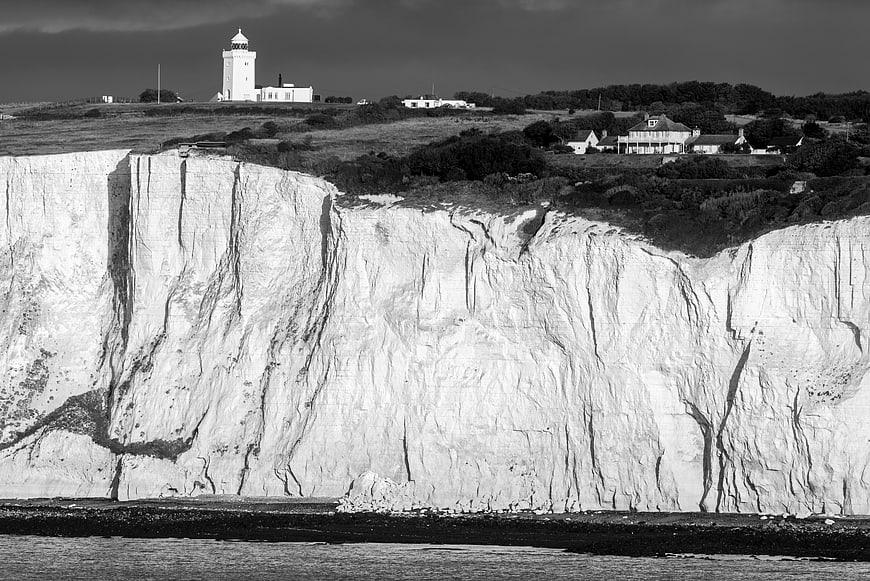 Black and white lighthouse on white chalk cliffs coastline