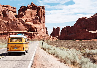 Yellow VW Bus Driving on Desert Road with Red Rock Formations