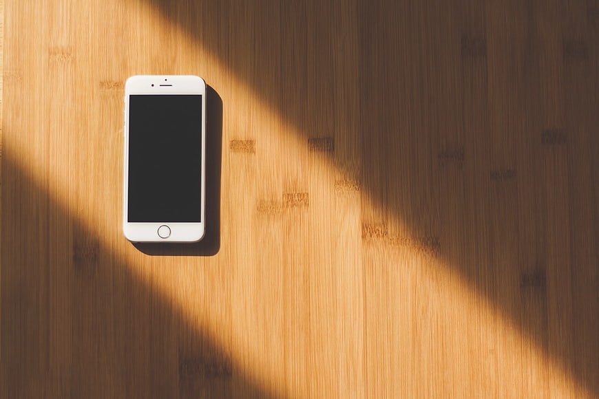 White Smartphone on Wooden Table with Sunlight Shadows