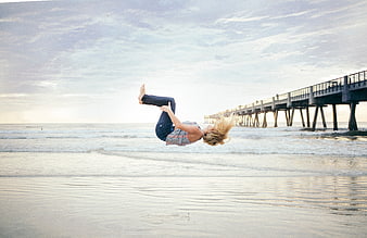 Woman jumping on beach with pier in background