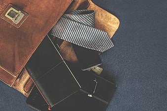Leather satchel with tie, wallet, and smartphone on blue background