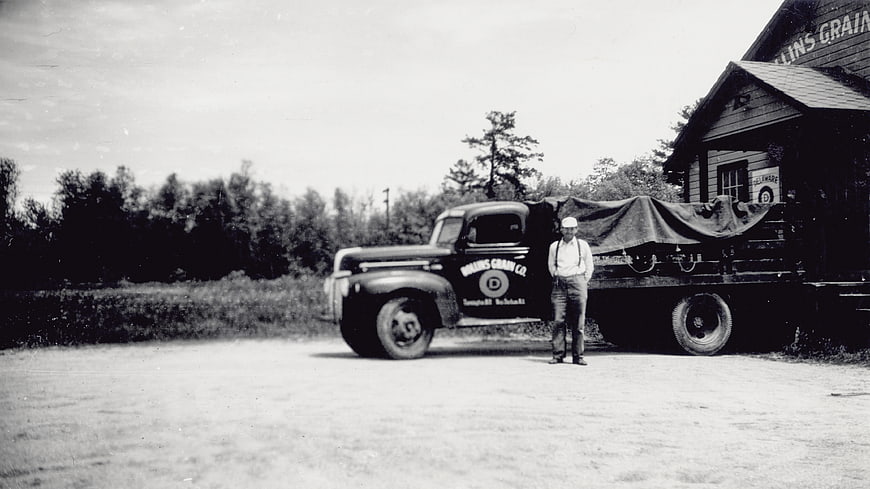 Vintage black and white photo of man standing by old truck