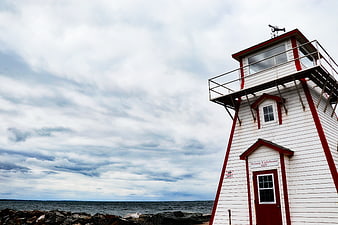 White and Red Lighthouse on Rocky Coastline Under Cloudy Sky