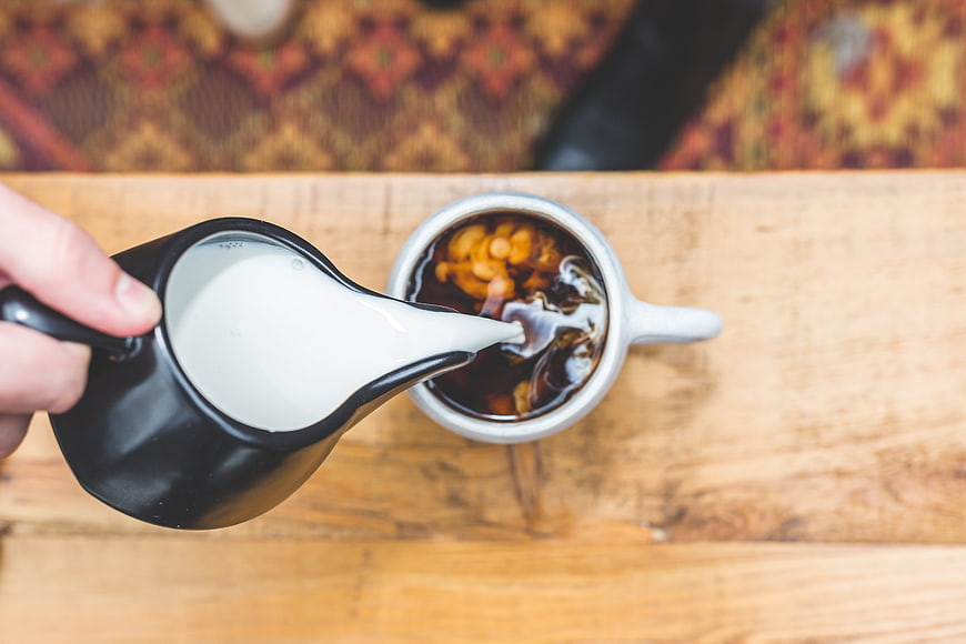 Overhead view of milk being poured into iced coffee cup