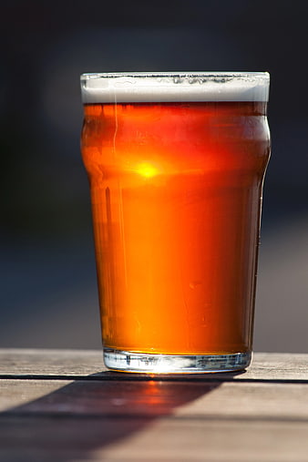 Glass of Amber Beer Backlit by Sunlight on Wooden Table