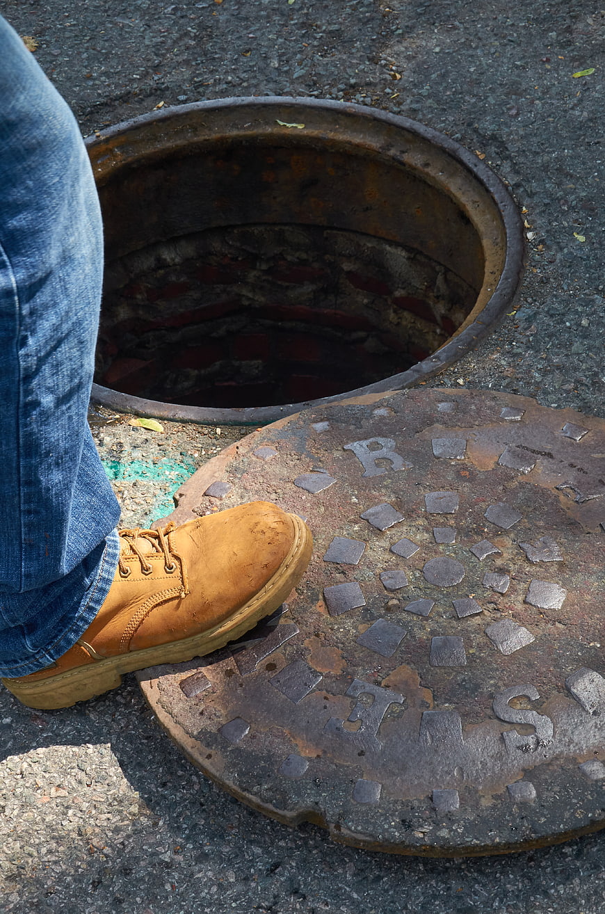 Worker boot on open manhole cover in street