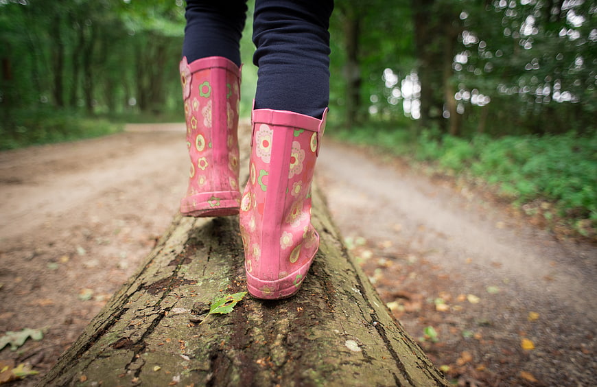 Child in pink floral boots walking on a log in forest