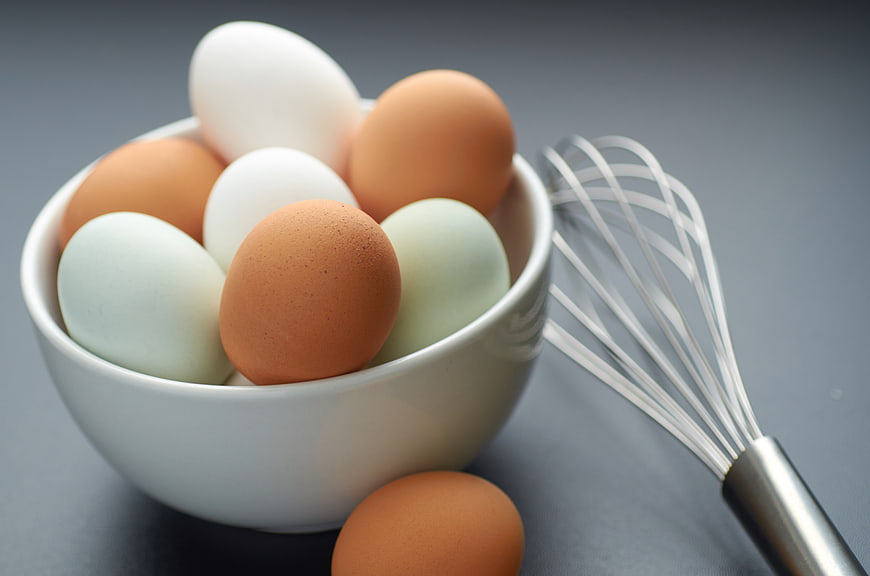 Colorful eggs in white bowl with whisk on gray background