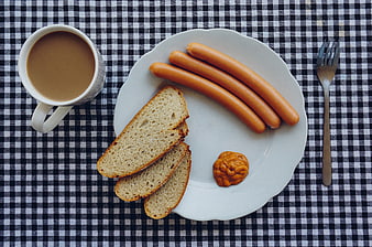 Top view of breakfast sausages, toast, and coffee on checkered tablecloth