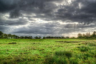 Dramatic storm clouds over green meadow with sun rays