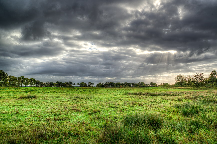 Dramatic storm clouds over green meadow with sun rays