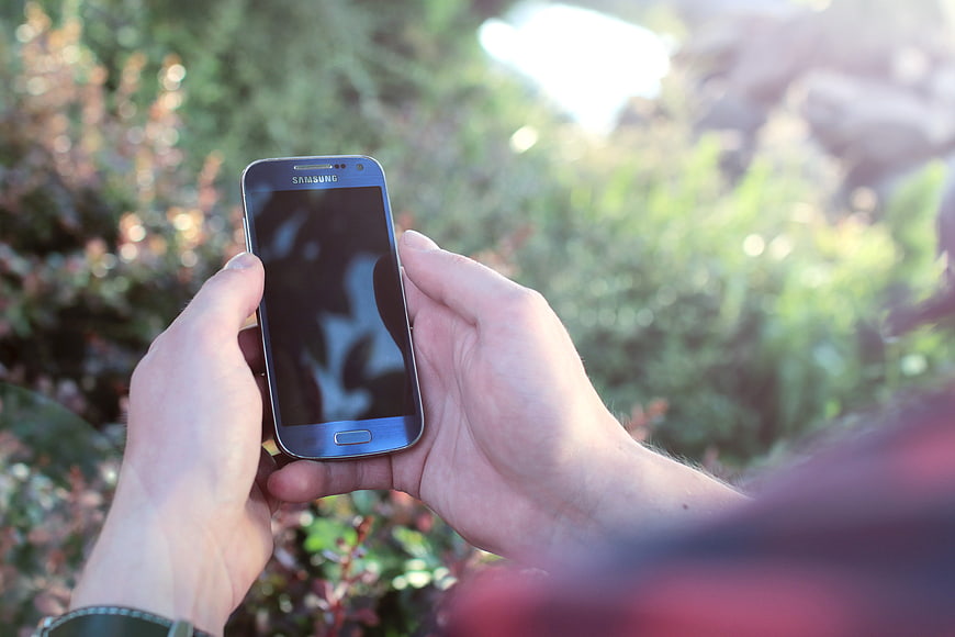 Hands holding smartphone in outdoor garden setting