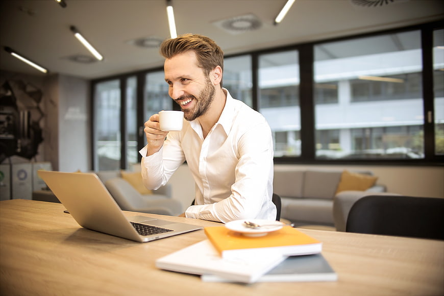 Smiling businessman drinking coffee at office desk with laptop