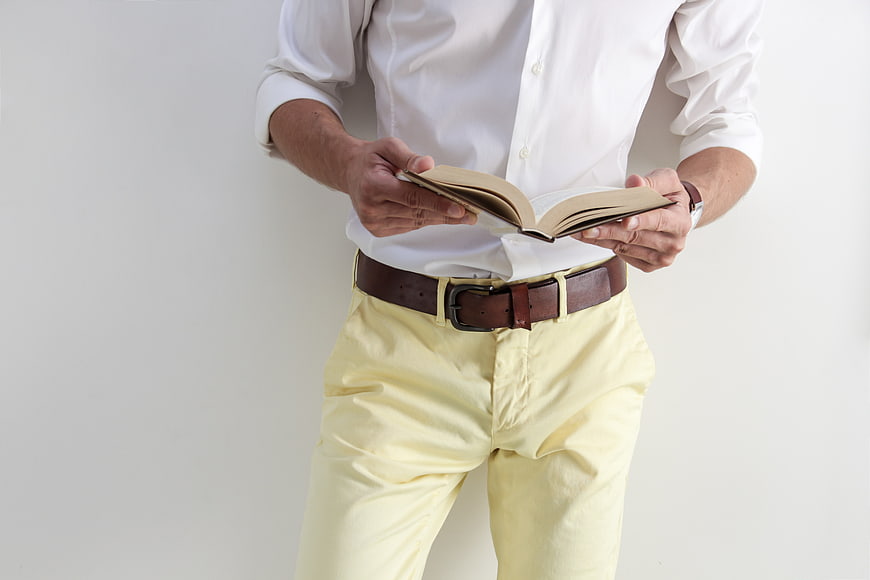 Man in white shirt and yellow pants reading a book