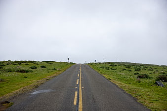 Empty asphalt road stretching through green grassy hills under overcast sky