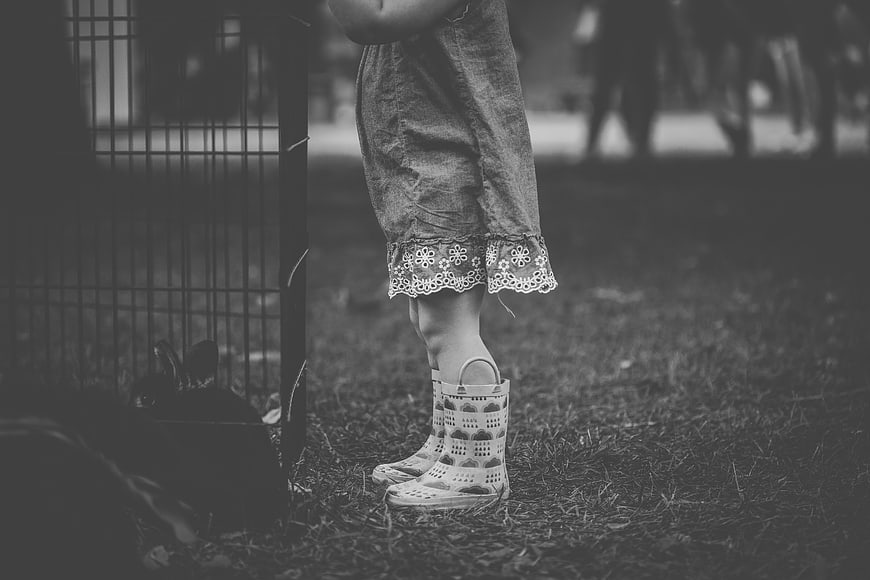 Child in Rain Boots Standing by Rabbit Cage