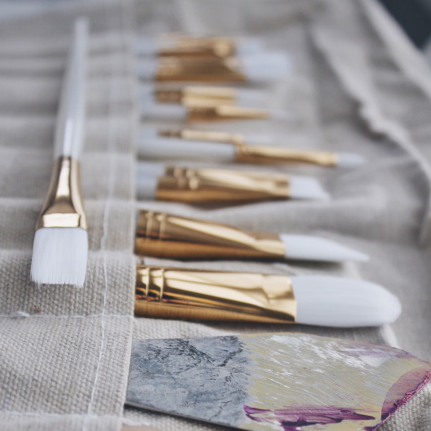 Gold and white paintbrushes on canvas with palette knife