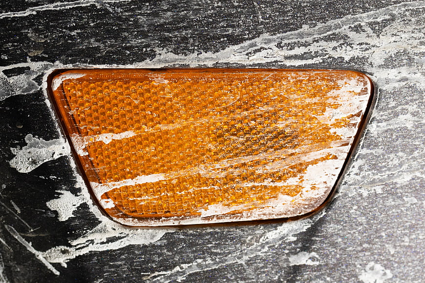 Close-up of orange car reflector covered in road salt and grime