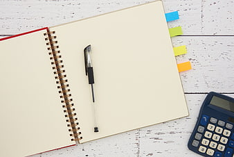 Flat lay of open notebook, pen, and calculator on white wood