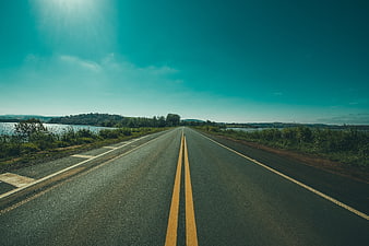 Empty asphalt road stretching toward horizon with lake and hills