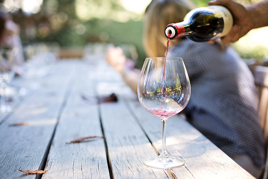 Red wine pouring into glass on rustic wooden table outdoors