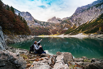 Couple hiking by alpine lake pointing at mountain peaks