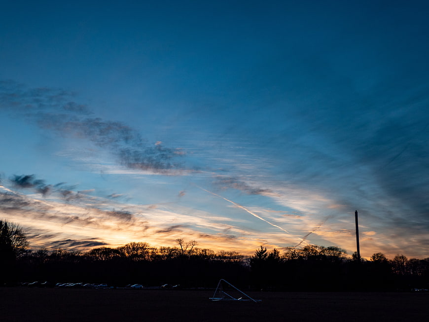 Dramatic sunset sky with contrails over silhouetted trees and field