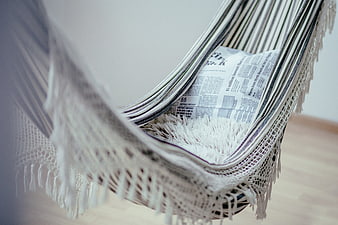 Close-up of a white macrame hanging chair with a newspaper