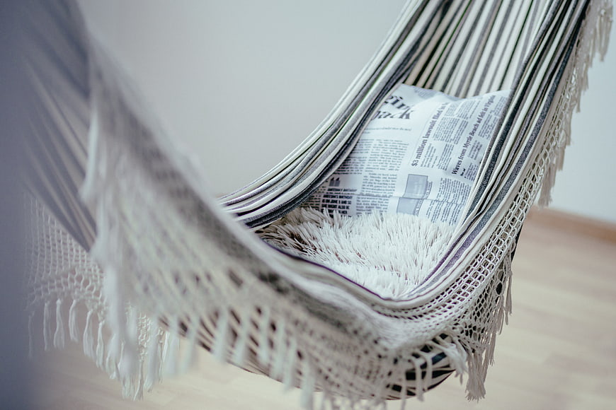 Close-up of a white macrame hanging chair with a newspaper