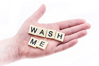 Hand holding Scrabble tiles spelling wash me on white background