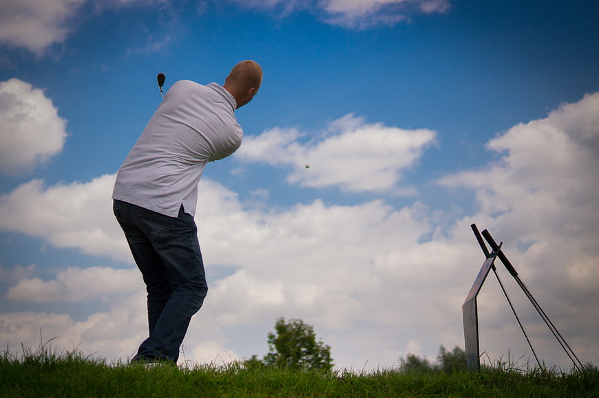 Golfer Swinging Club on Grass Hill Against Blue Sky
