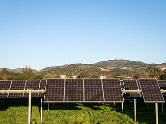 Solar panels in a green field with hills and blue sky