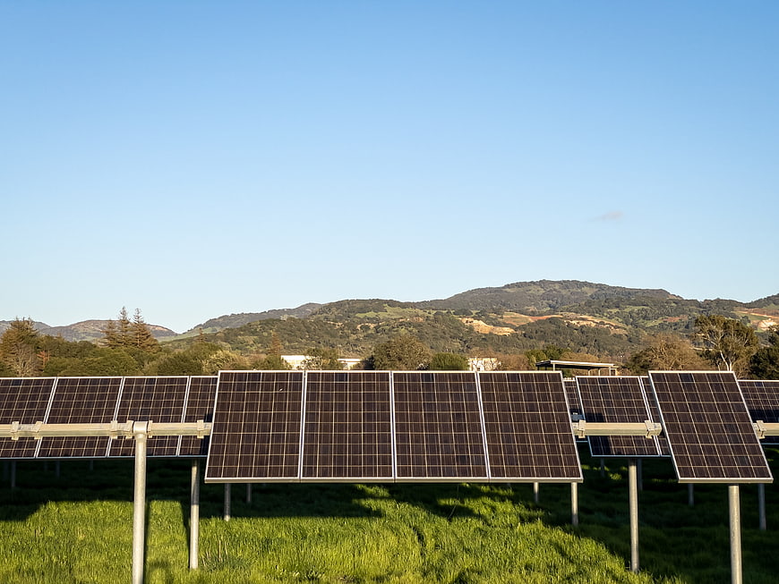 Solar panels in a green field with hills and blue sky