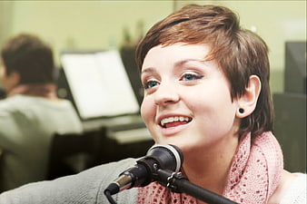Young woman singing into microphone in recording studio