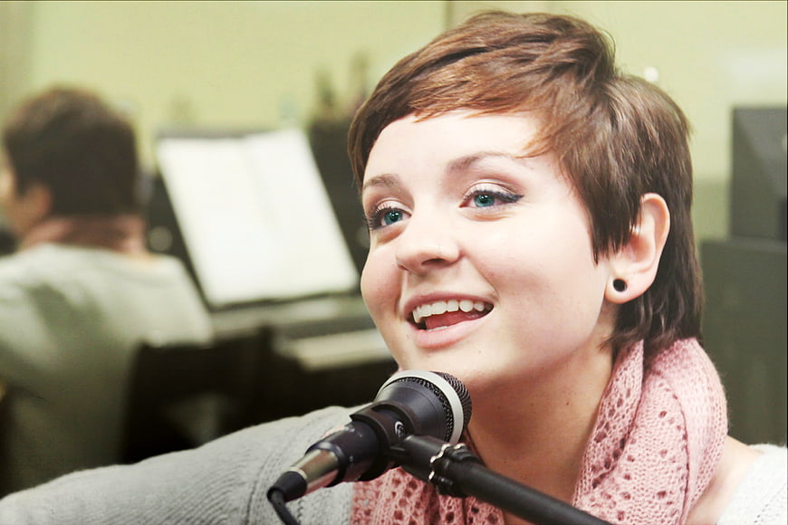 Young woman singing into microphone in recording studio